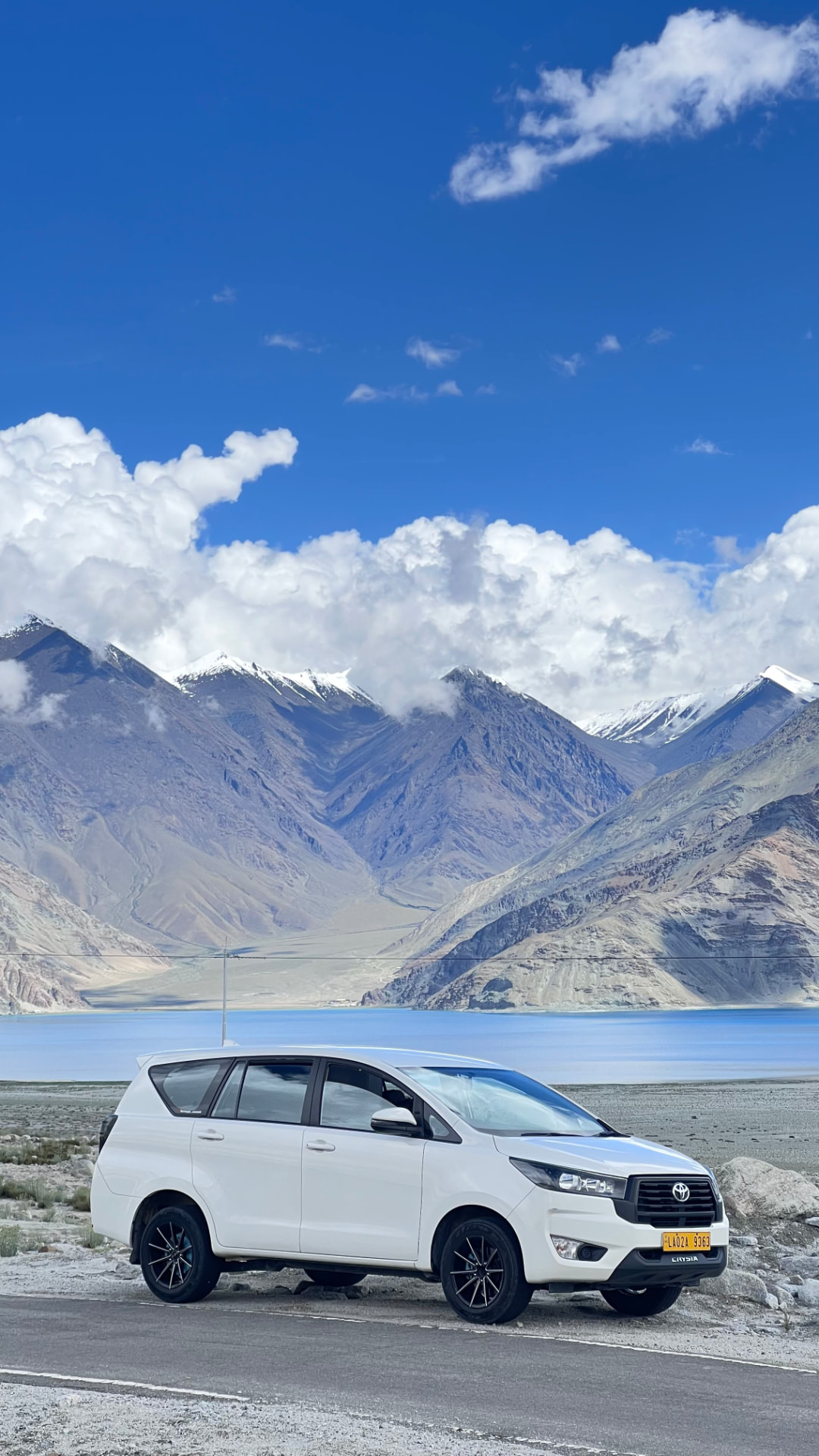 White Innova Crysta beside Pangong Lake with snow peaks