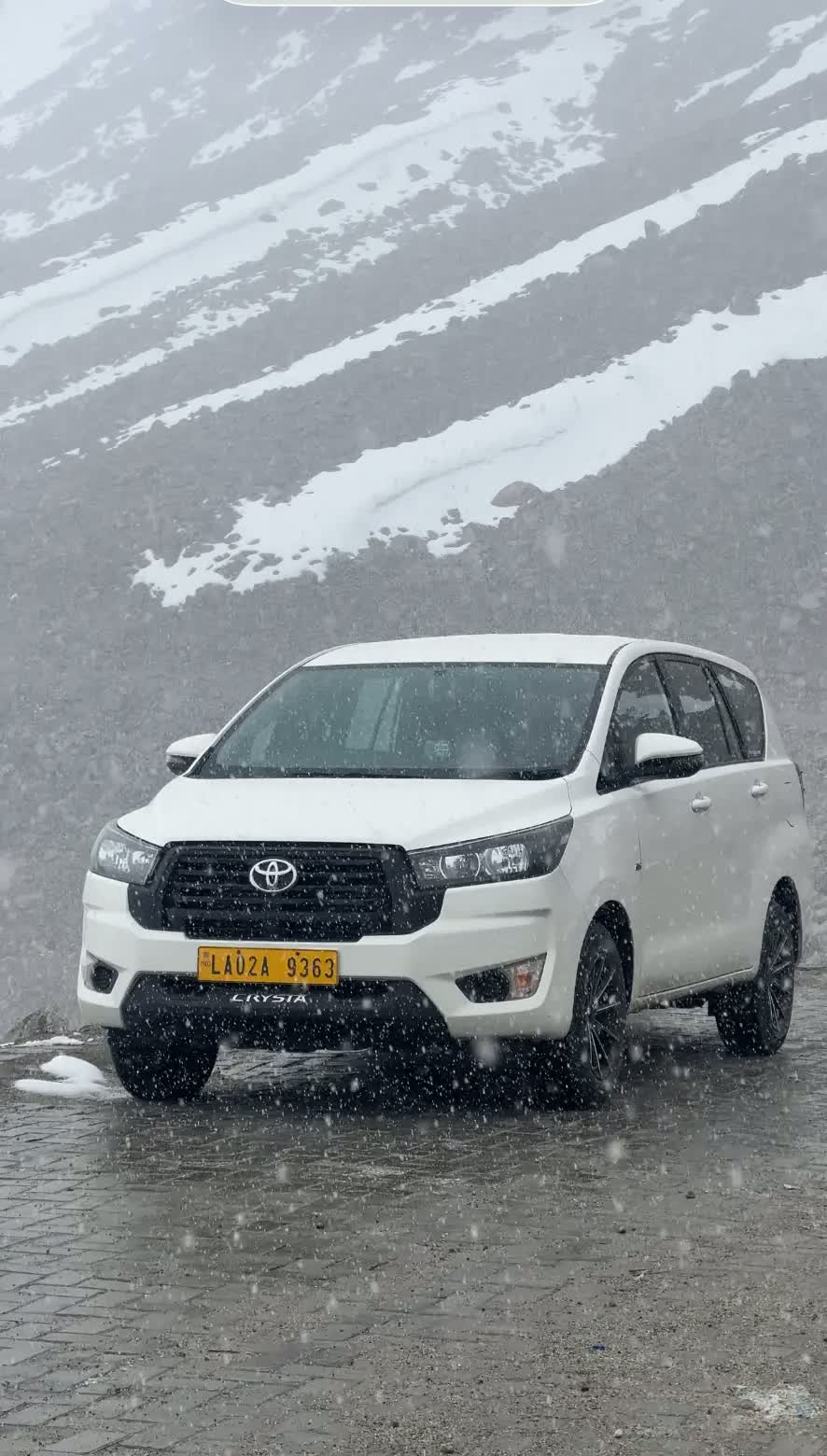 White Innova Crysta during snowfall on a Ladakh mountain road